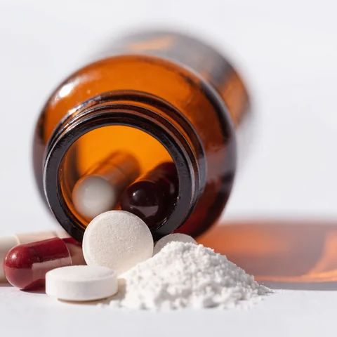 Cápsulas, comprimidos e pó farmacêutico ao lado de frasco âmbar
